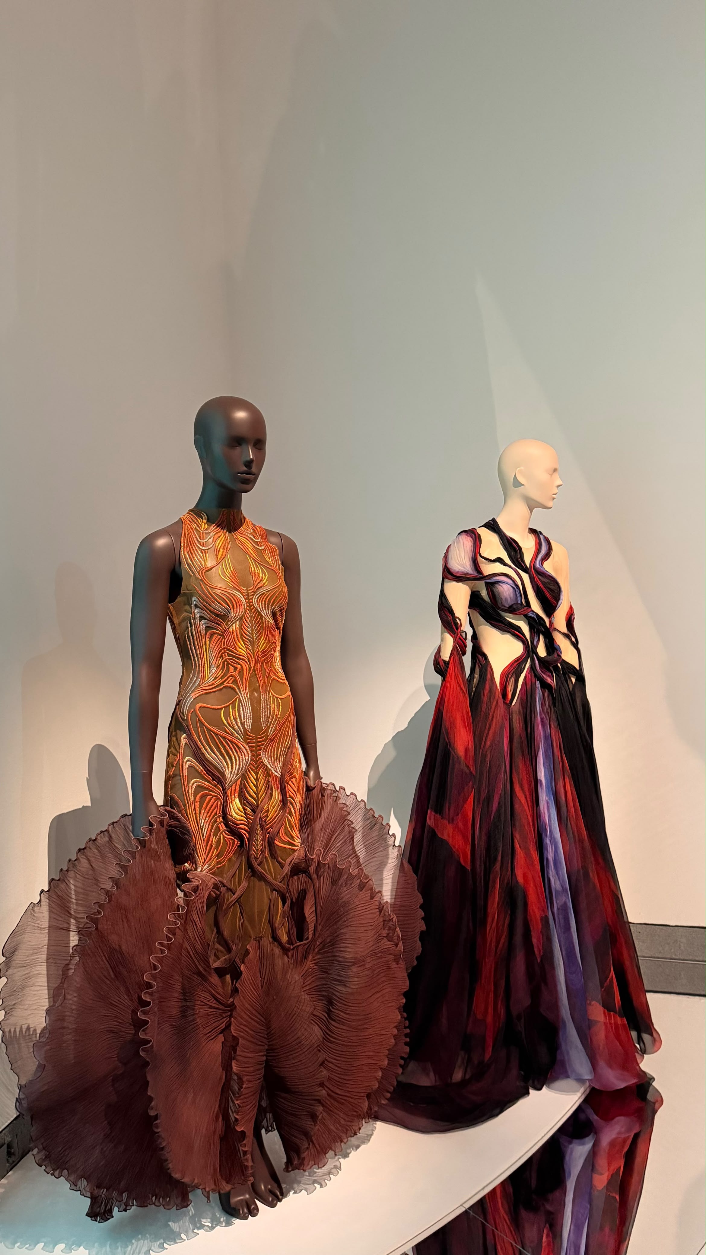 Two Iris van Herpen designs in orange, burgundy and violet on display at Brooklyn Museum