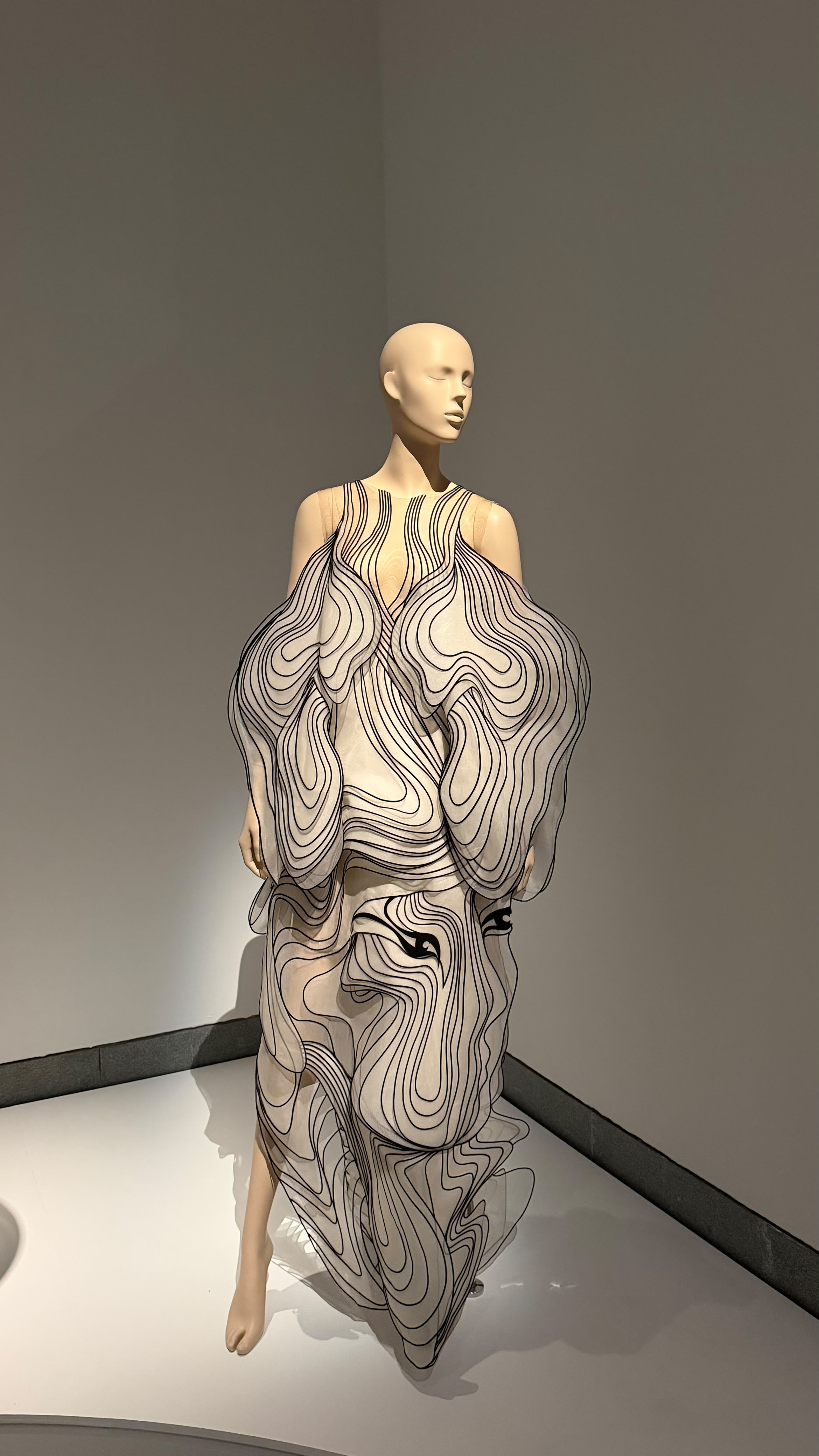 An Iris van Herpen design with flowing dark lines across a pale sculptural dress
