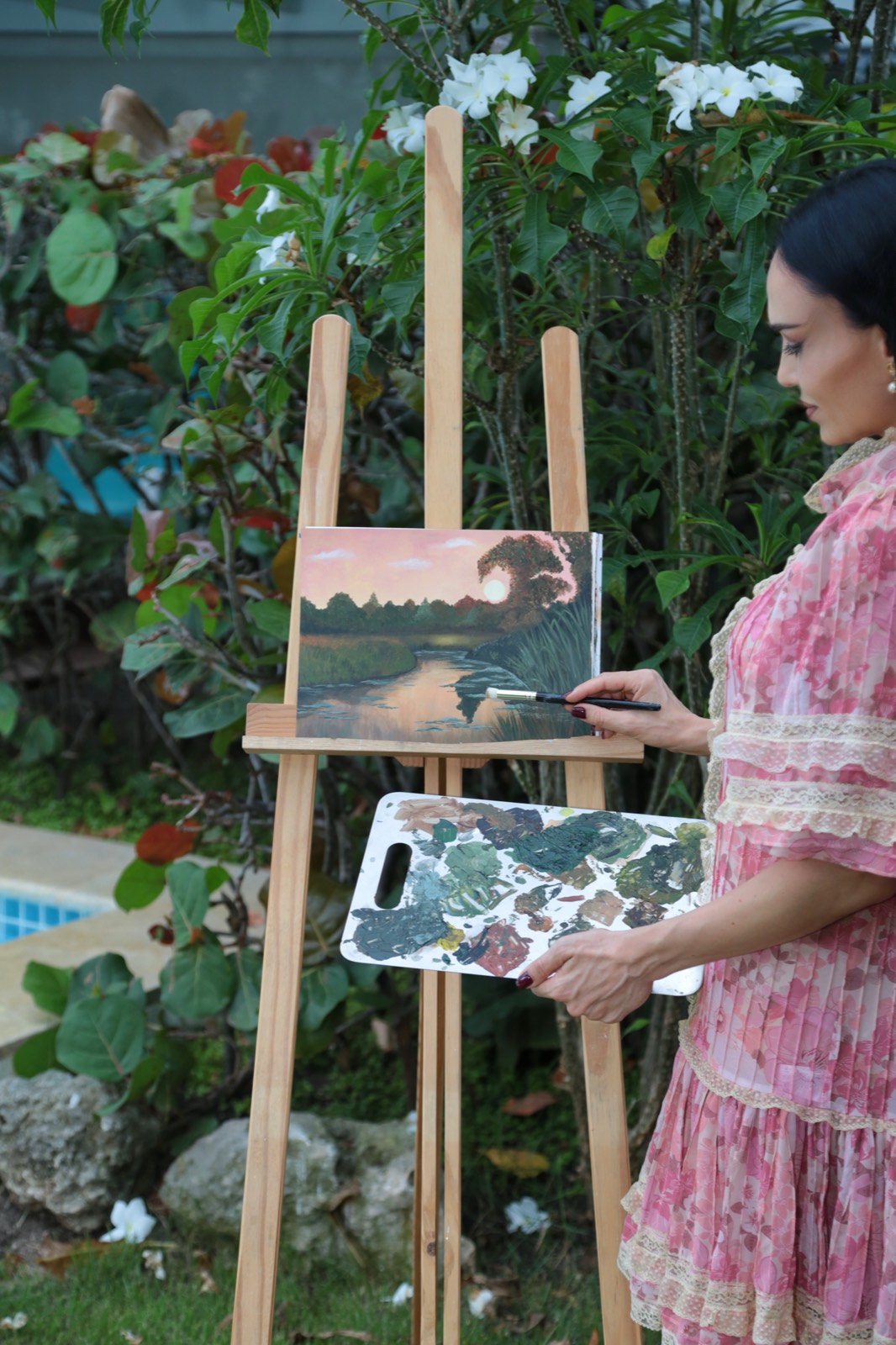 Galina painting at an easel surrounded by garden flowers